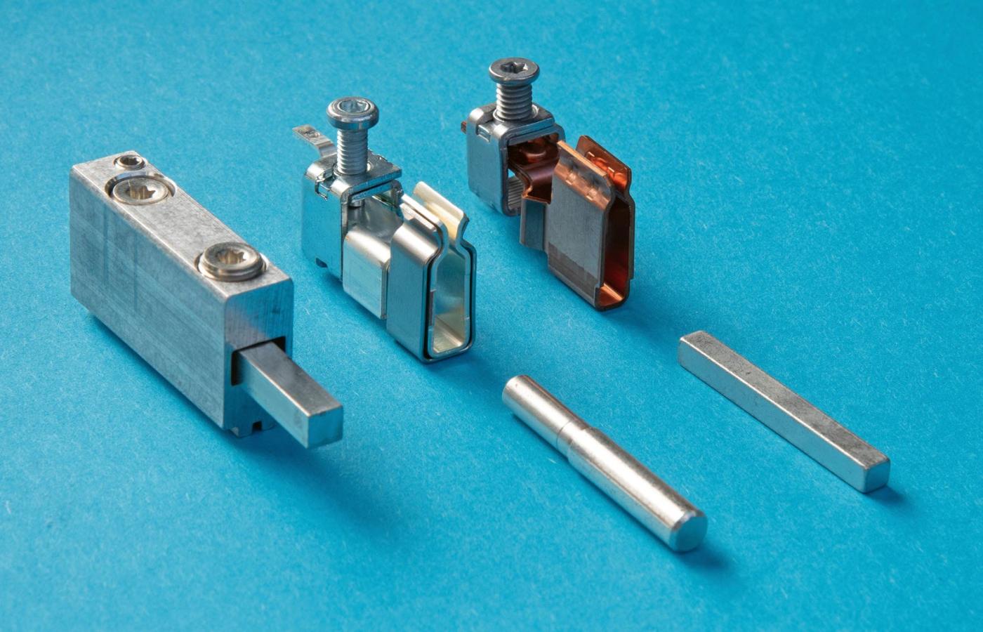 Die Kontakte der drei Hersteller im Vergleich. Links der Schraubkontakt der Anschlussklemme von Seidl. Er besteht aus einem korrosionsbeständigen Aluminiumprofil (Aluminium-Composite-Werkstoff). In der Mitte der Federkontakt von Hager, gebogen aus einer mit Silber beschichteten Kupferlegierung. Eine Klammer aus Federstahl verstärkt die Federkraft. Rechts der Federkontakt von Eweco, ebenfalls aus einer korrosionsbeständigen Kupferlegierung. Der im Bild sichtbare Clinchpunkt stellt konstruktiv die Stabilität/Federkraft sicher.